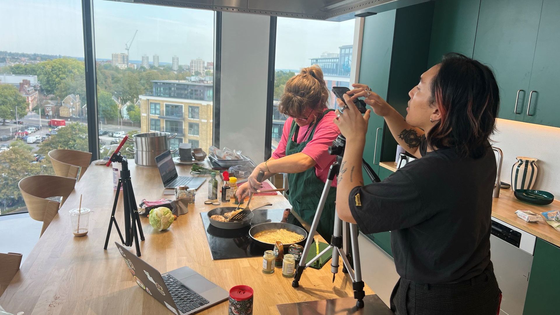 Two people film a cooking demonstration in a modern office kitchen.