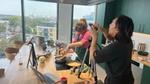 Two people film a cooking demonstration in a modern office kitchen.