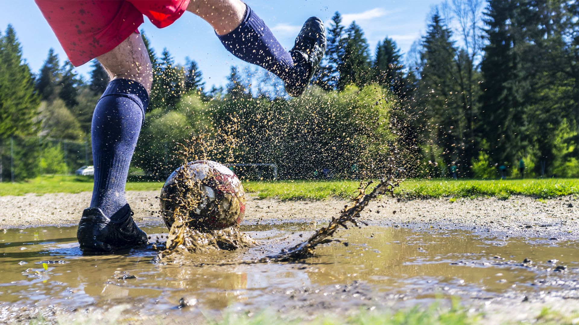 Someone kicking a football in a muddy puddle.