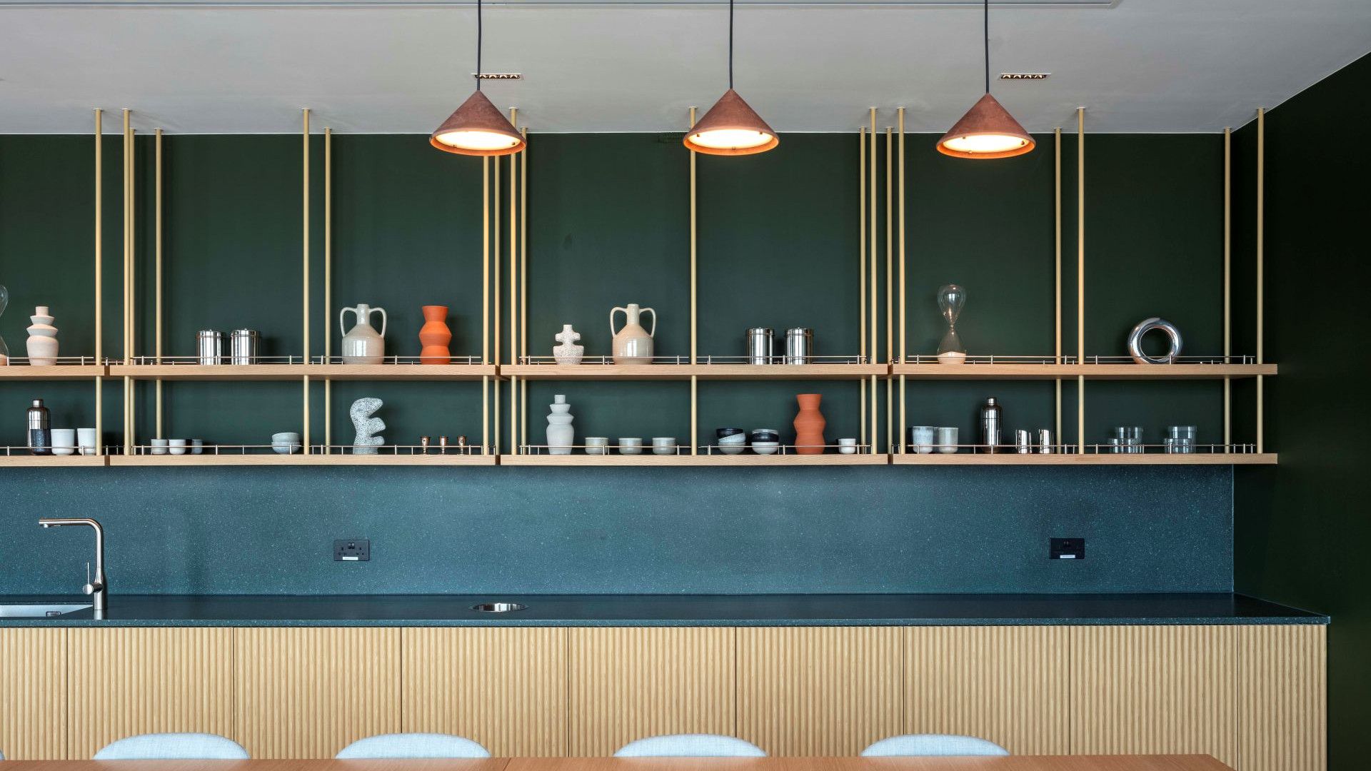 Modern office kitchen with open shelving, decorative ceramics and three pendant lights.