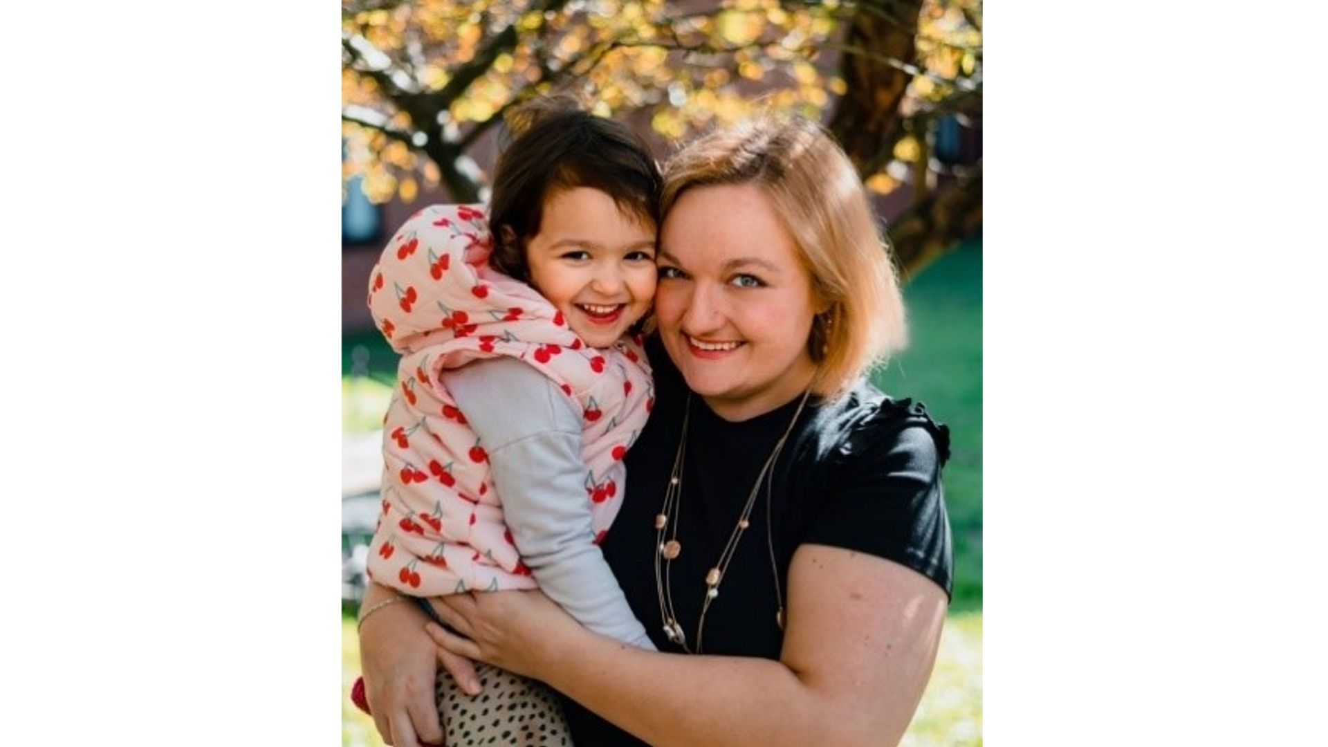 Lauren wearing a black t-shirt, carrying her daughter and both smiling