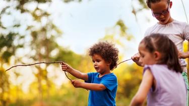 Three children holding sticks, out in a forest.