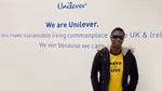 Ademola standing next to the Unilever logo on the wall inside of the Leatherhead office