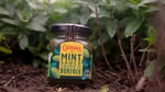 A jar of Colman’s mint sauce in front of green plants.