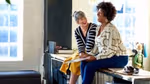 Two women sitting on a worktop chatting and laughing.