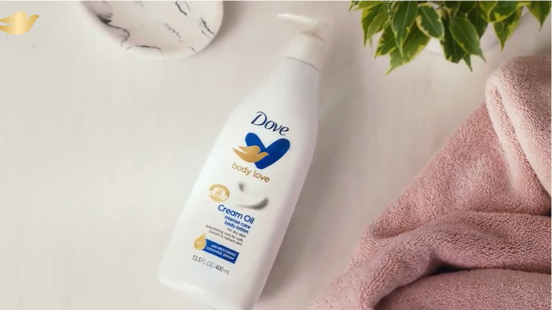 Dove Body Love Cream Oil lotion bottle beside pink towels and green leaves.