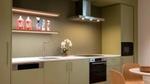 Modern fitted kitchen with green cabinets, integrated appliances and cleaning products displayed on a shelf.