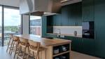 Modern office kitchen with dark green cabinets, a wooden island, bar stools and floor-to-ceiling windows.