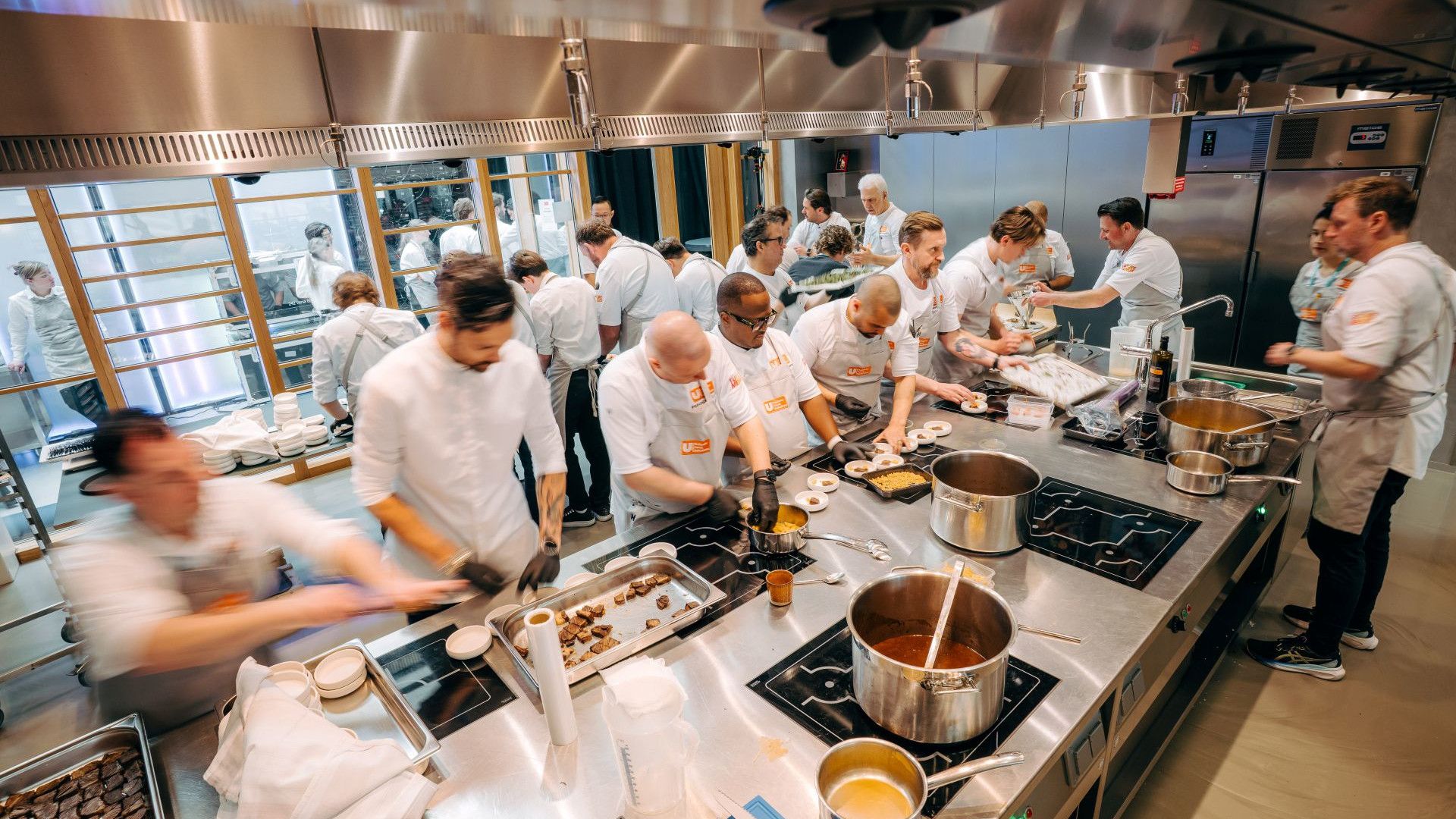 A team of Unilever Food Solutions chefs in a busy kitchen prepare food. Various pans can be seen on stovetops.