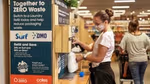 Woman filling a plastic bottle from an in-store refill machine that dispenses Surf and OMO products.