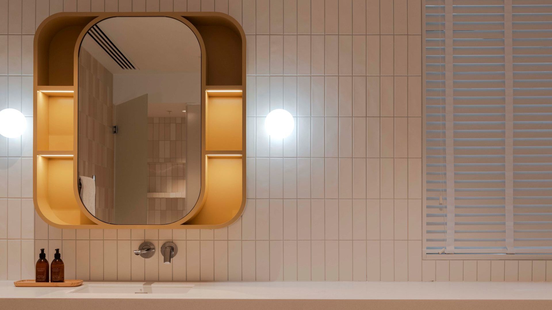 Modern bathroom vanity with a rounded mirror, illuminated shelves and white tiled walls