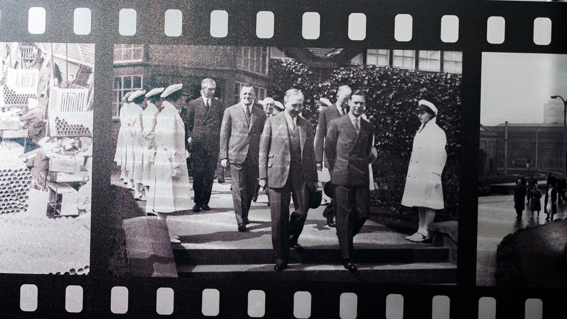 Historic filmstrip shows suited officials touring a facility as uniformed staff stand in line.