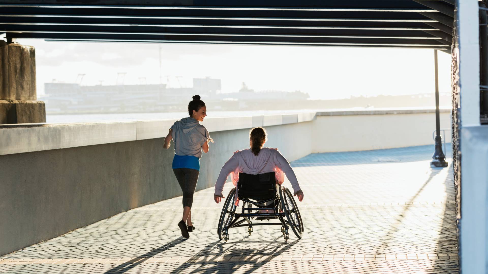 Woman running next to a person in a wheelchair under a bridge