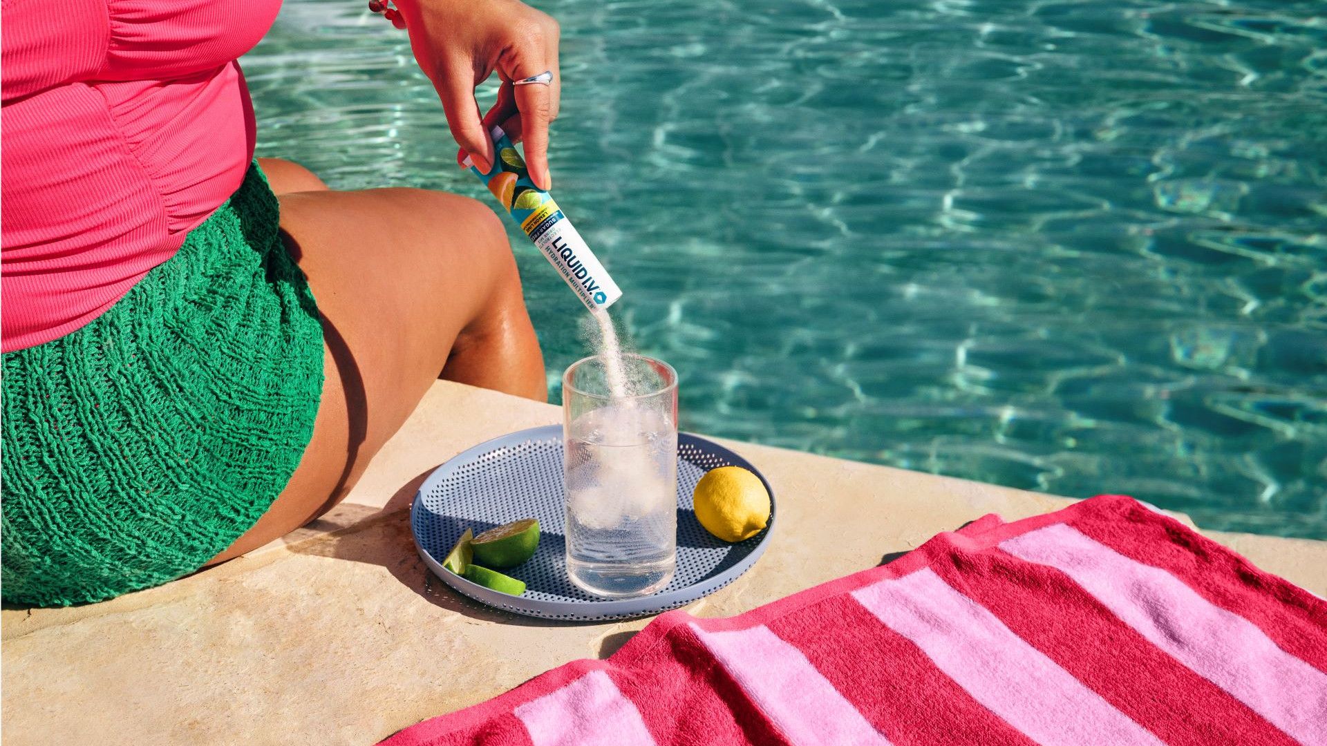 Lady sitting beside a swimming pool pouring Liquid I.V powdered hydration mix into a glass of water